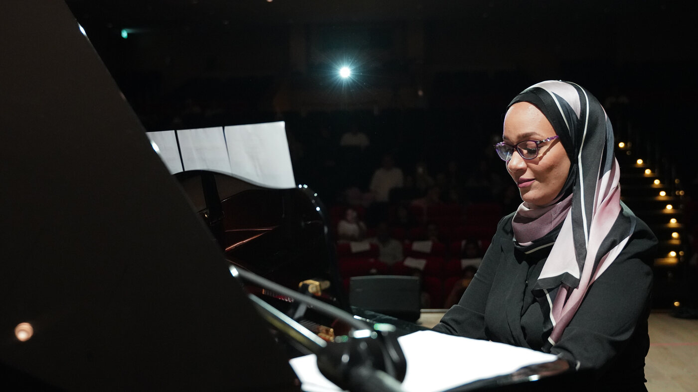 Yasmin Shennawy seated at a grand piano as the audience takes their seats